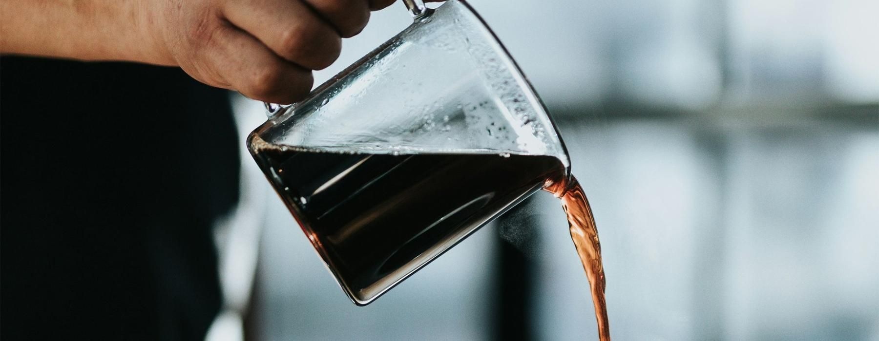 a person pouring a carafe of coffee into a cup
