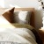 swath of sunlight shines across a well made bed and bedside table with a vase of cotton plants